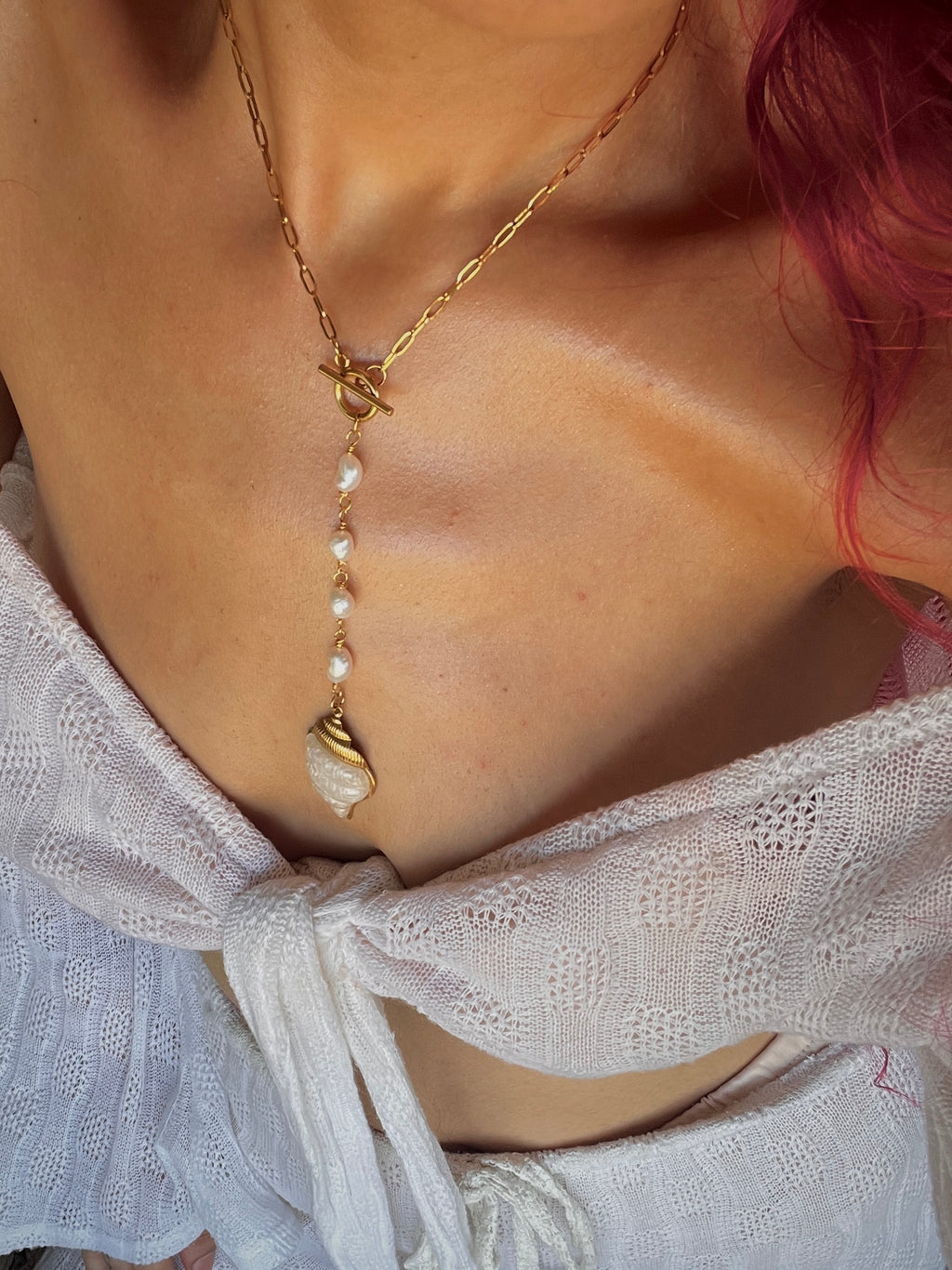 Necklace with pearls and gold chain worn by a person with red hair, wearing a white lace garment.