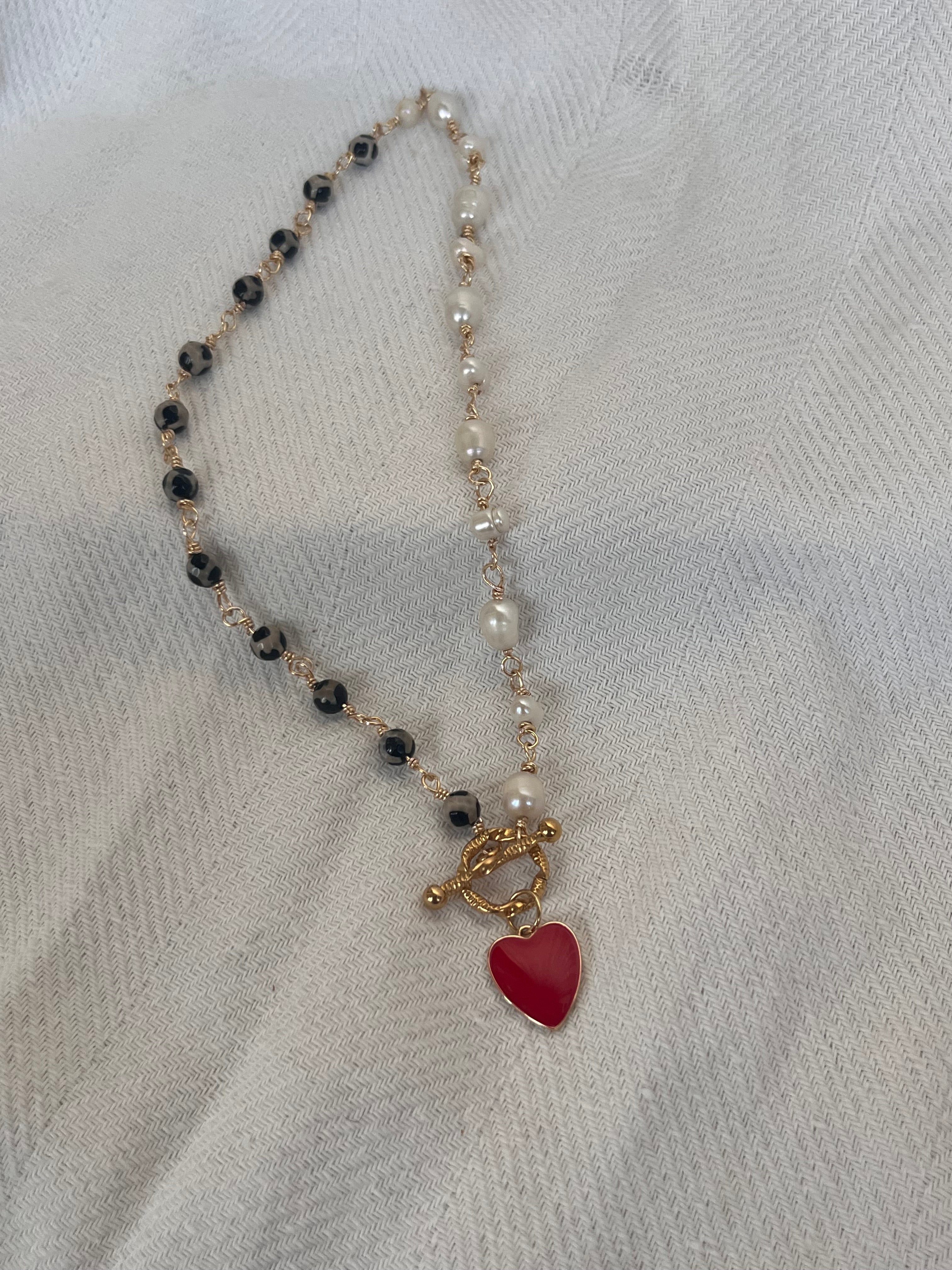 Necklace with pearls & leopard beads and a red heart charm on a white fabric background