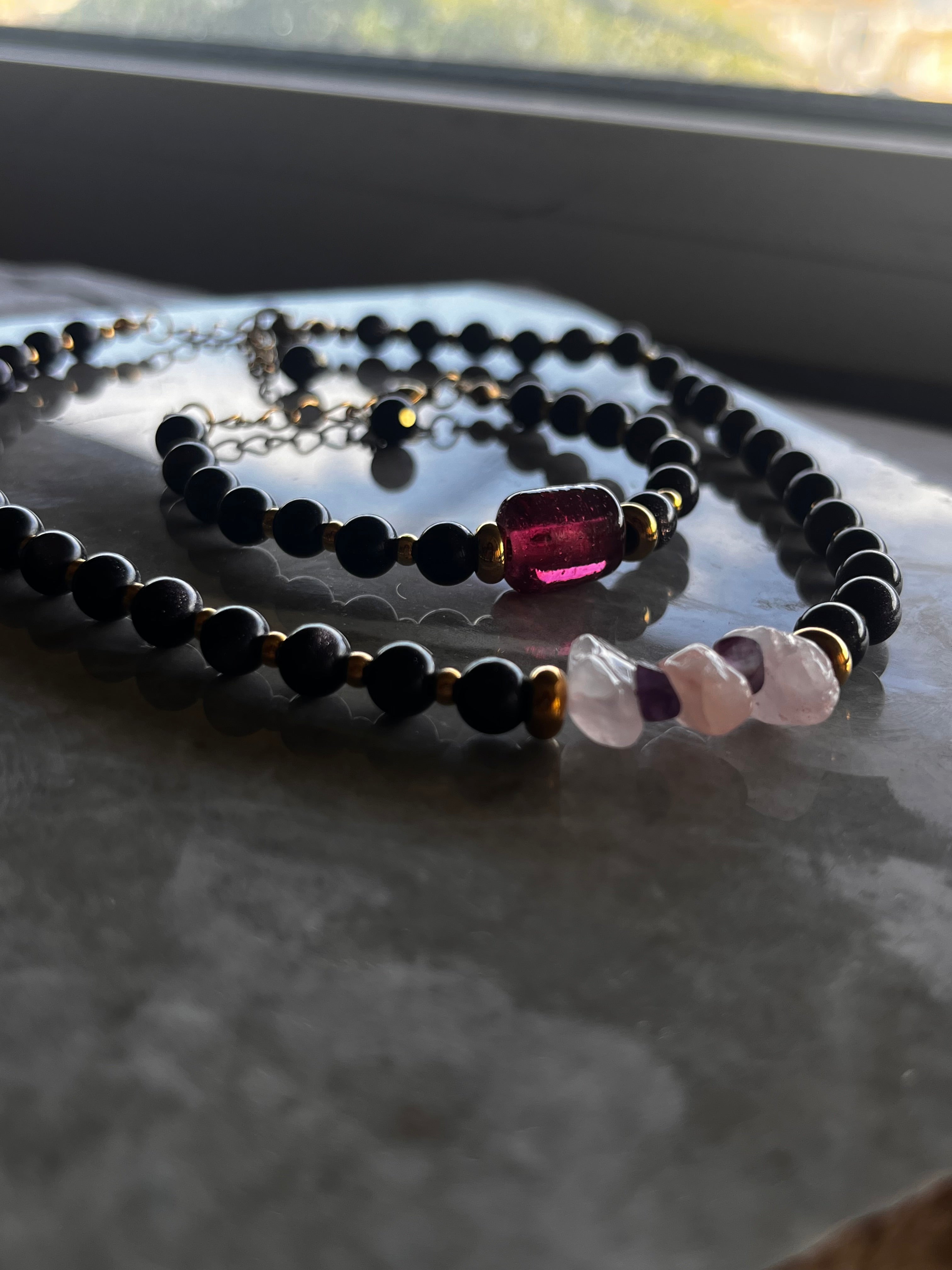 Close-up of a beaded necklace with black, gold, and multicolored beads on a textured surface.