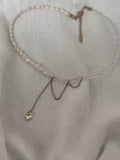 Handmade asymmetric necklace featuring white pearls, faceted crystals, and a crystal heart pendant on a soft white fabric background.