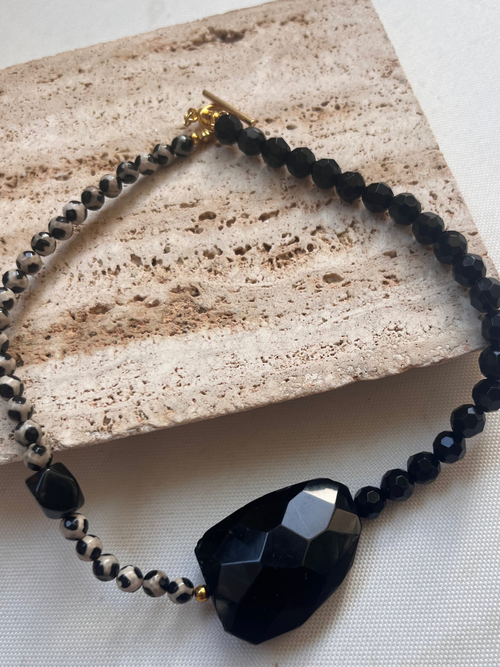 Black beaded necklace with a large faceted black stone on a textured surface