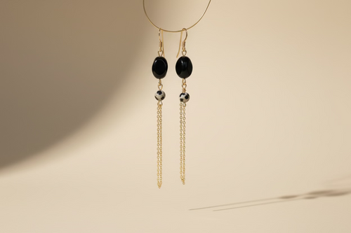 Gold earrings with black beads on a beige background