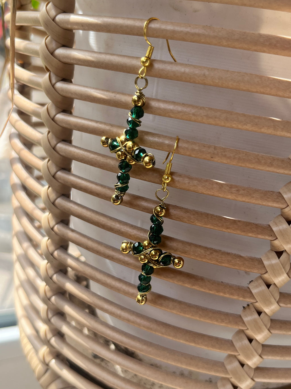 Gold and green beaded cross earrings on a woven surface