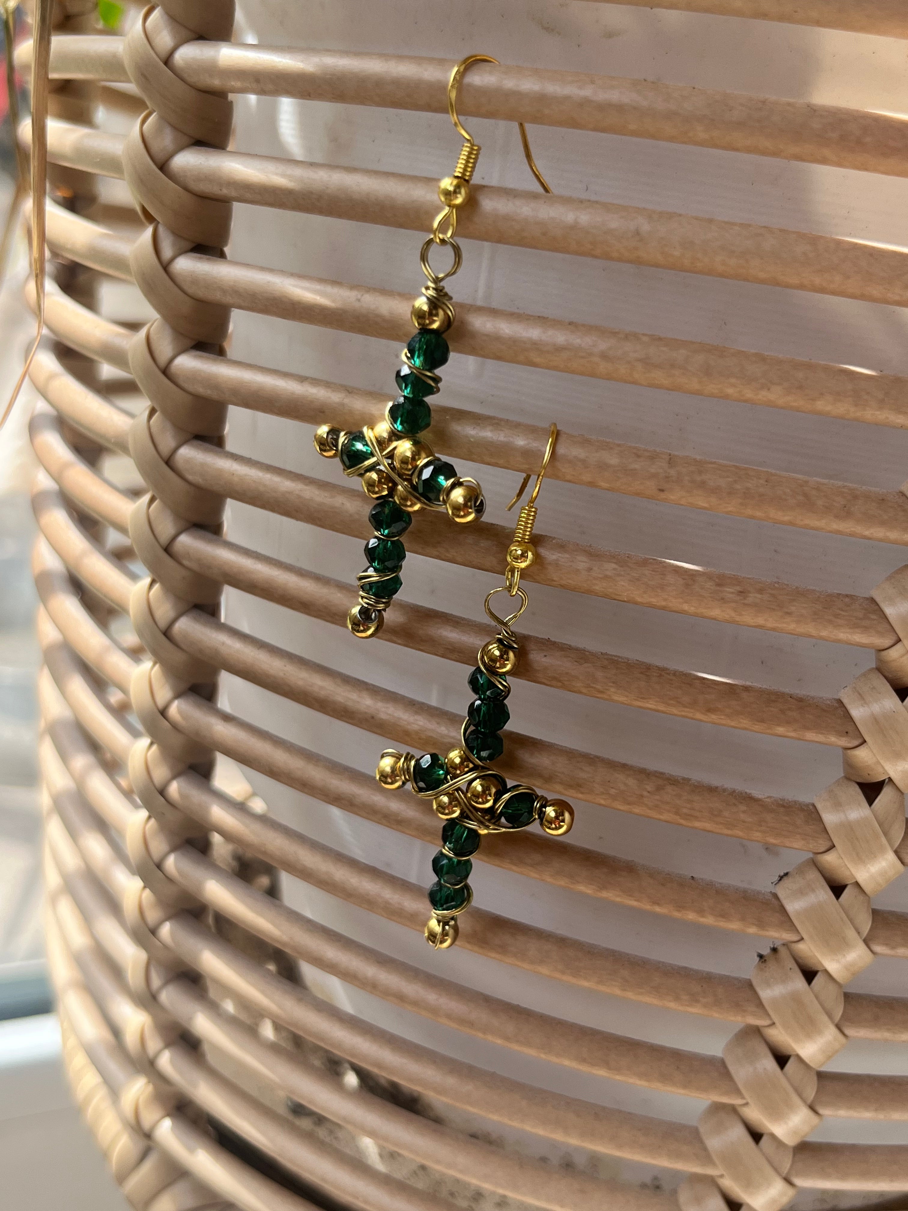 Gold and green beaded cross earrings on a woven surface