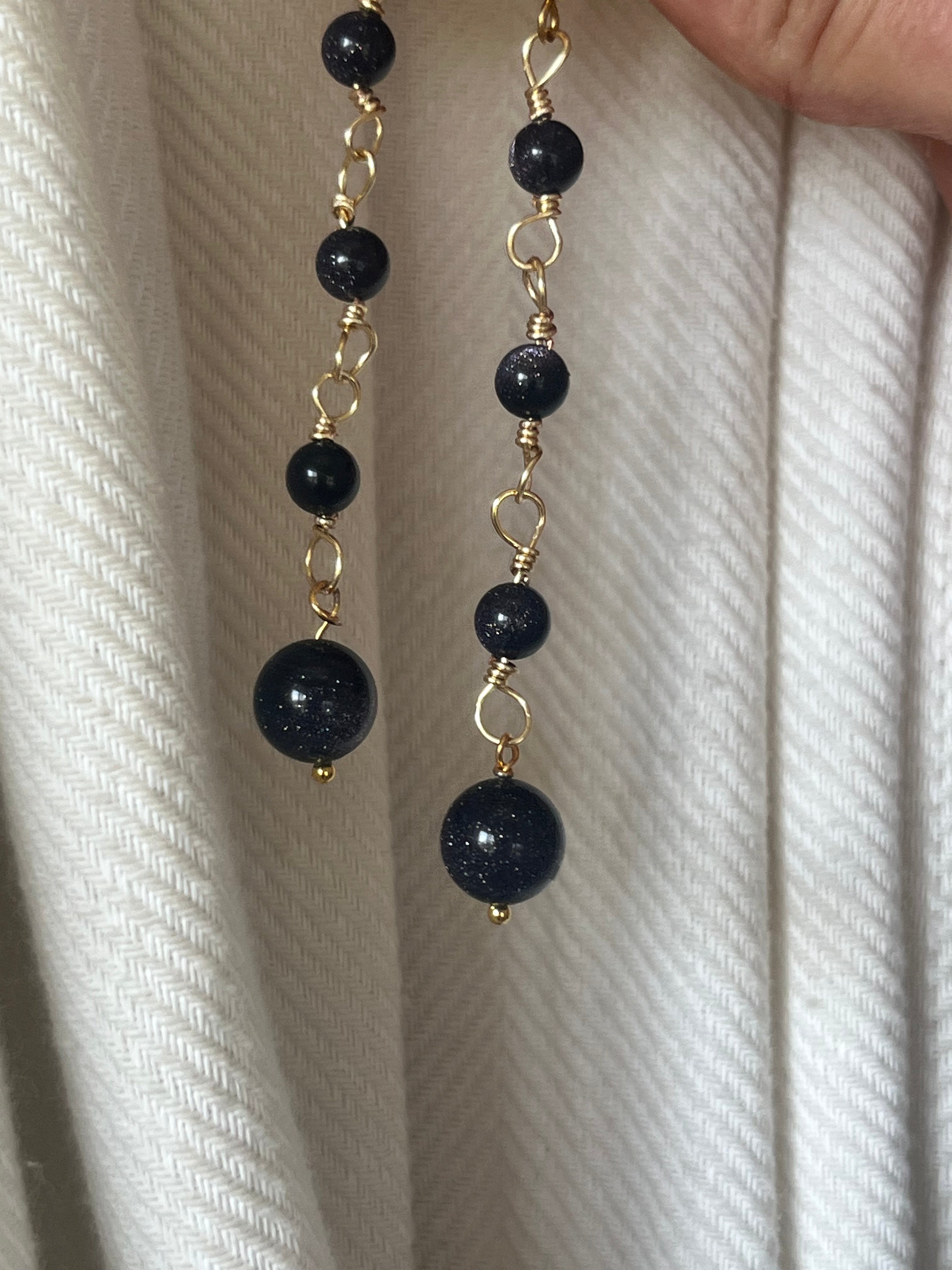 Black beaded earrings with gold accents held against a white fabric background
