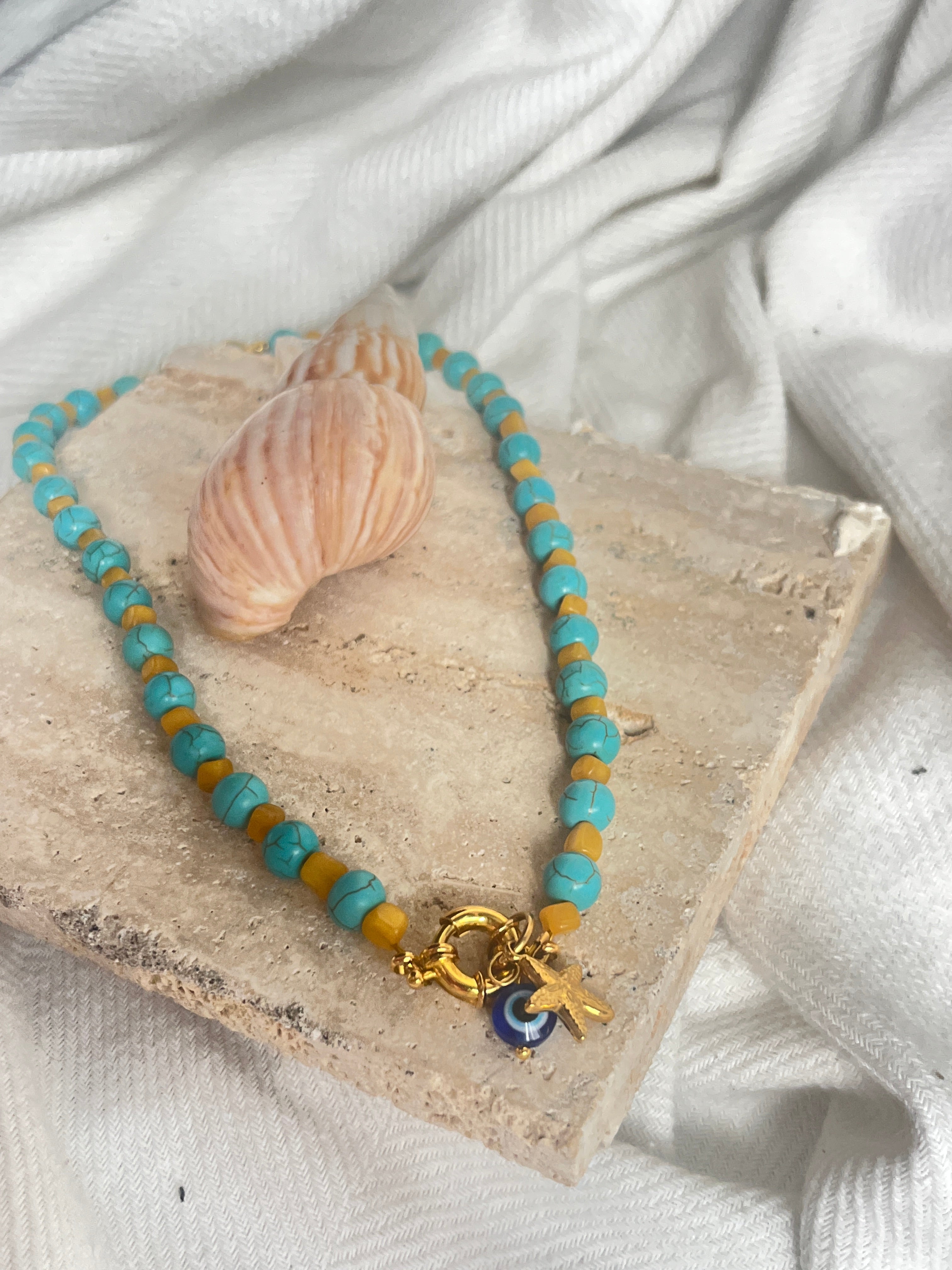 Necklace with turquoise and gold beads on a stone surface with a shell