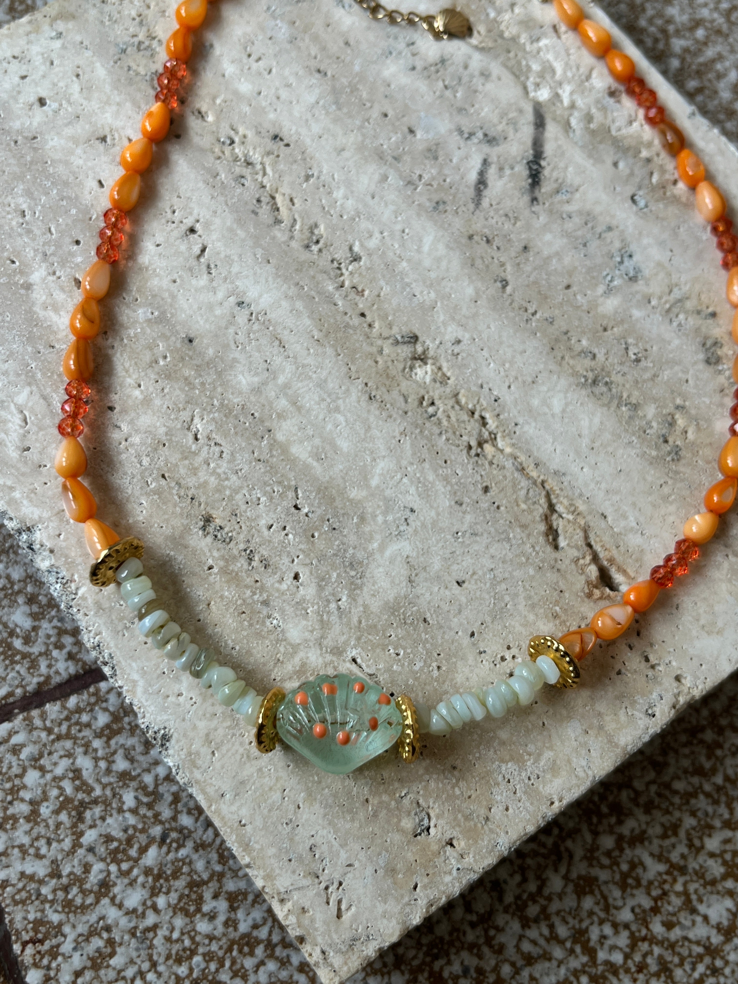 Necklace with orange and green beads on a textured surface